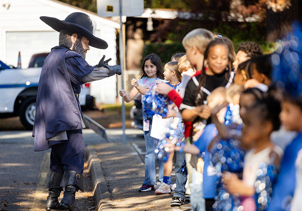 CNU mascot reaches out to fist-bump Riverside Elementary students holding blue pom-poms along the street.