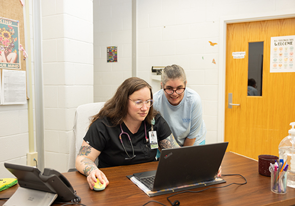 Two medical professionals at a desk looking at a laptop.